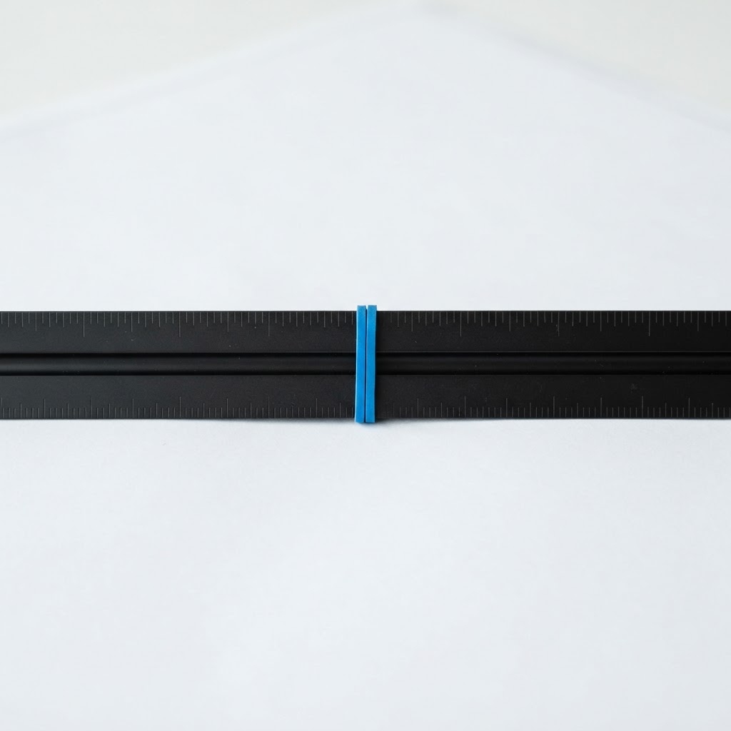 A matte black scale ruler on a white desk with an electric blue rubber band