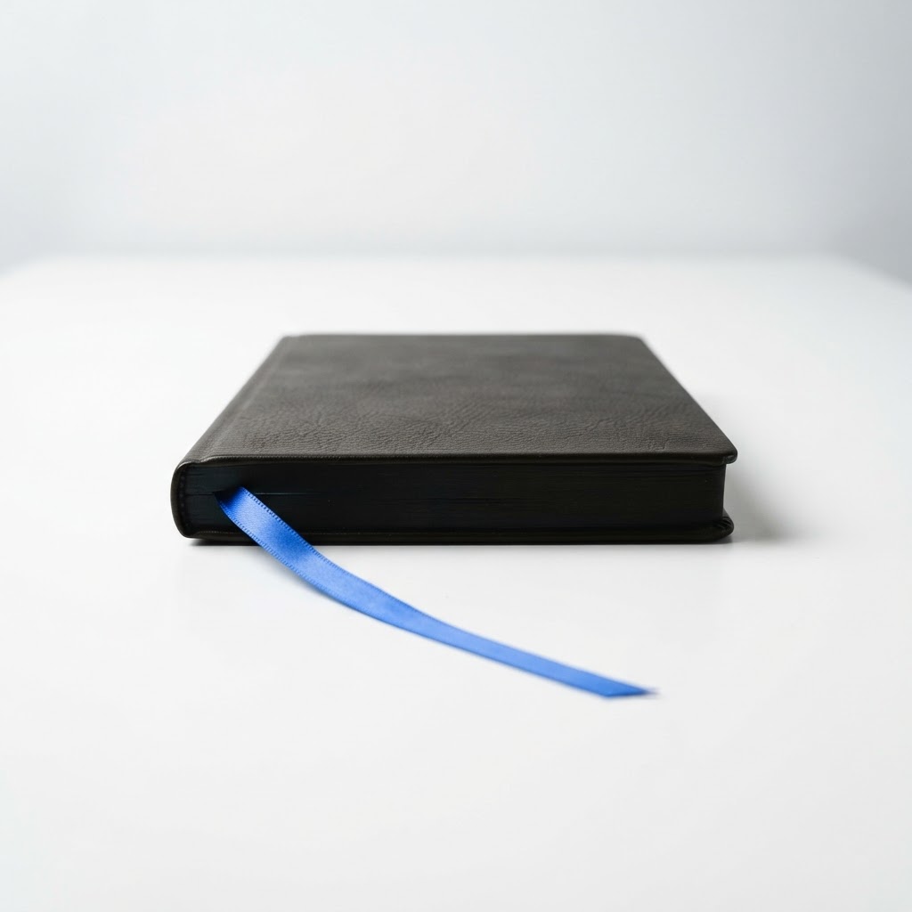 A black leather journal on a white desk with a blue bookmark
