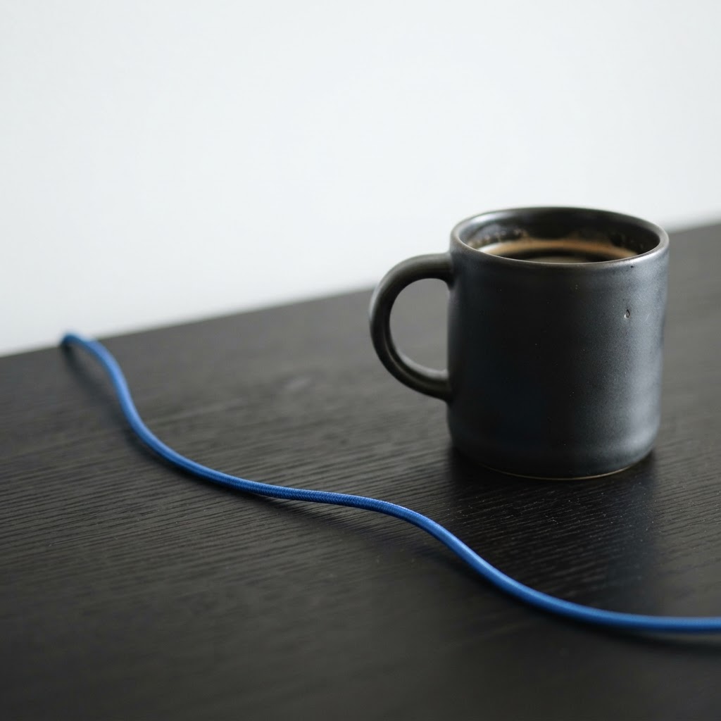Close up of a mug and blue cable on a dark desk surface