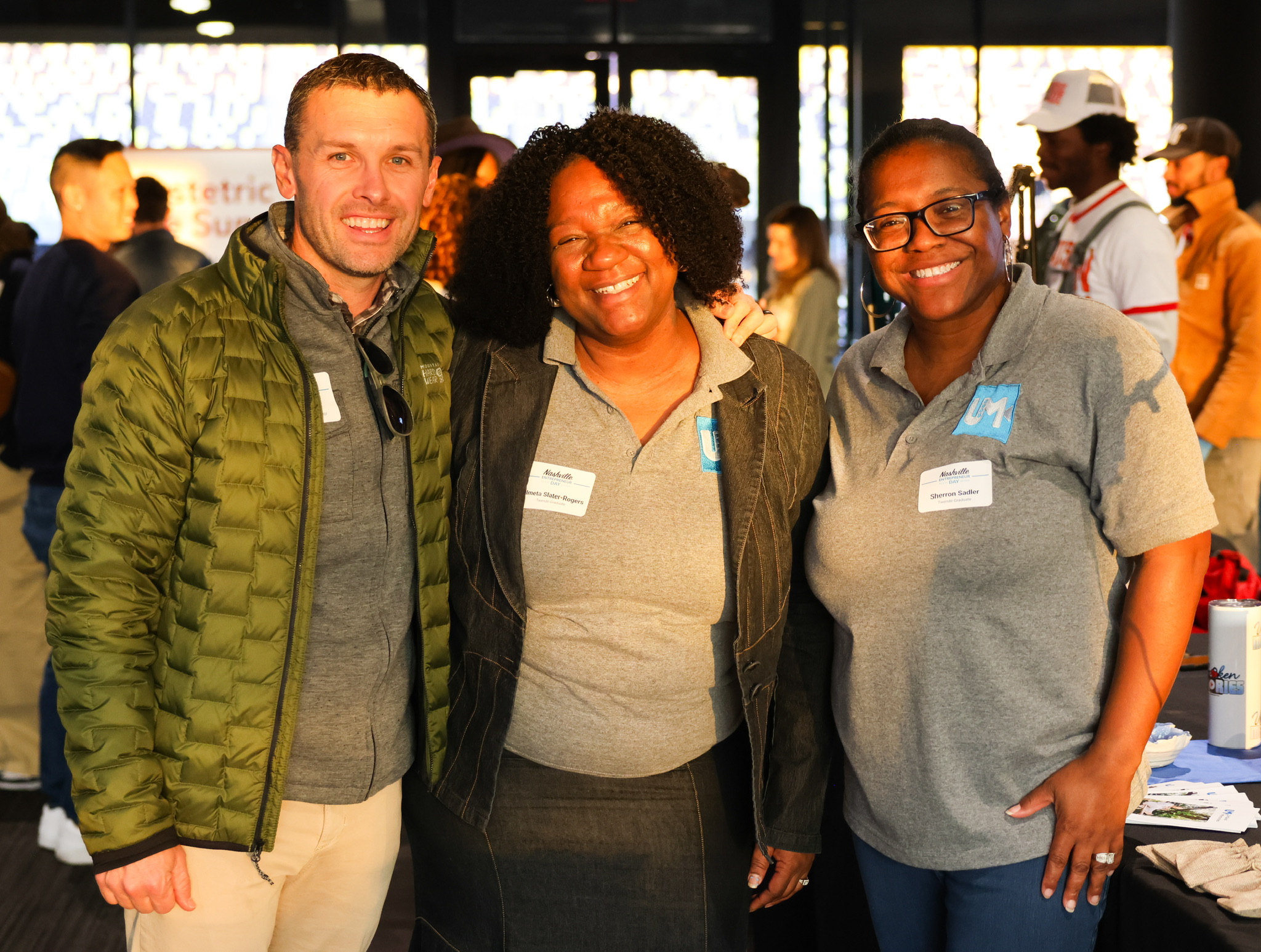 Three colleagues smiling together at a professional event in a well-lit indoor space.