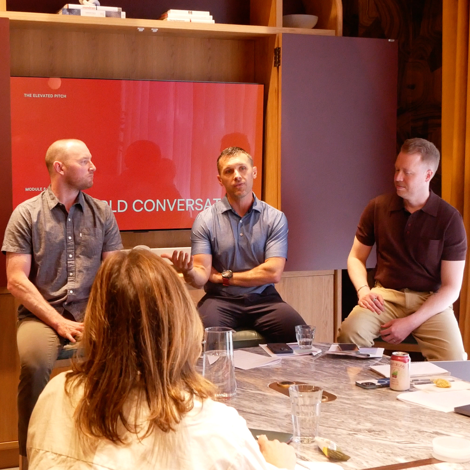 Three men sitting in a semi-circle during a discussion, with a woman's back visible in the foreground.